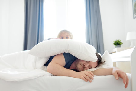 Little child awake. Early in the morning he wakes up his sleeping father in bed at home. Tired dad hears nothing, sleeps and does not wake up. Parenthood. Tired and burnout parents.の写真素材