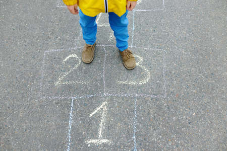 Little boy's legs and hopscotch drawn on asphalt. Child playing hopscotch game on playground on spring day. Outdoors activities for children.の写真素材
