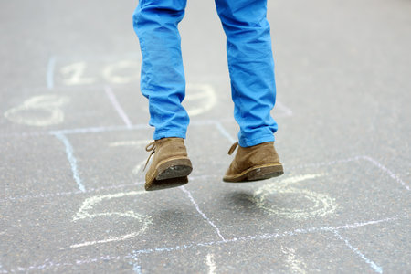 Little boy's legs and hopscotch drawn on asphalt. Child playing hopscotch game on playground on spring day. Outdoors activities for children.の写真素材