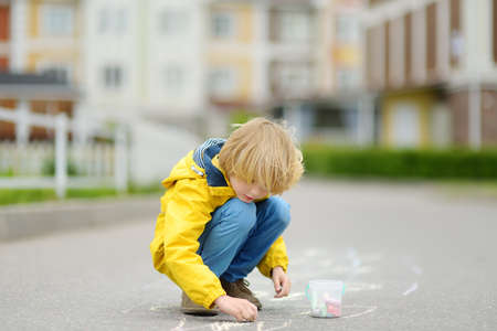 Little kid boy drawing hopscotch with colored chalk on asphalt. Child playing hopscotch game on playground outdoors on a spring day. Outdoor activities for children.の写真素材