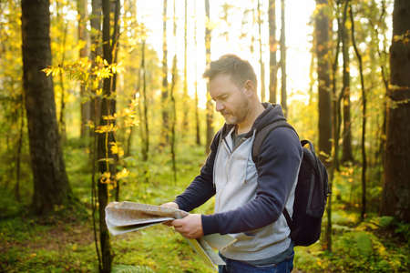 Mature man tourist is hiking. Person looking map during orienteering in sunny autumn forest. Volunteer is searching for people lost in woodland. Outdoors adventure, hike, extreme.の写真素材