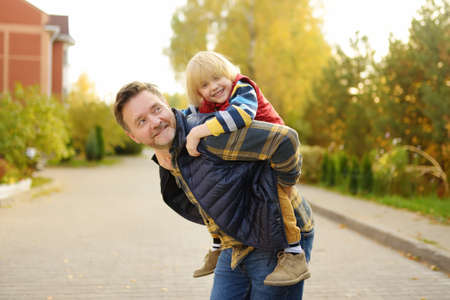 Little boy and his father having fun during stroll on sunny autumn day. The father rides the child...