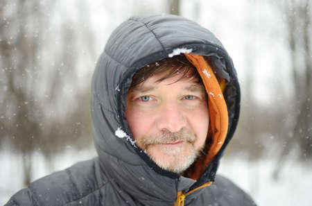 Portrait of mature man during hiking in winter forest. Wintertime outdoor vacation. Snowfall