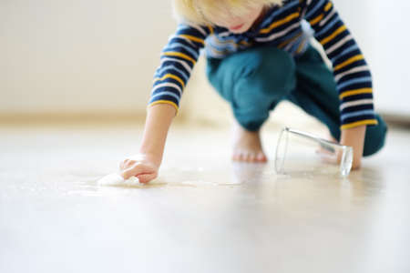 Little boy wipes water spilled from a glass on the floor. Teaching a child to clean up after himself. Responsibility, accuracy. Help around the houseの写真素材