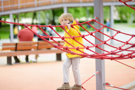 Cute preschooler boy having fun on outdoor playground. Spring summer autumn active sport leisure for kids. Activity for family with children. Equipment for entertainment park for kids.の写真素材