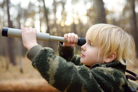 Little boy scout with spyglass during hiking in autumn forest. Child looking through a spyglass....
