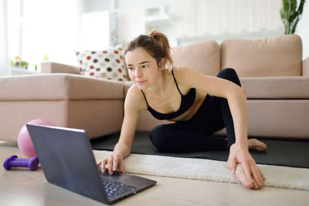 distance sports fitness training. An attractive young woman does yoga or stretching online using a...