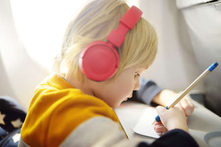 Cute little boy traveling by an airplane. Child using player to listen to a music or audiobook...