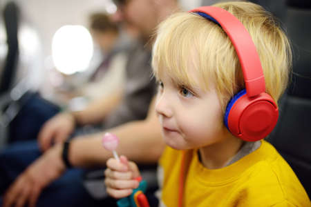 Cute little boy traveling by an airplane. Child using player to listen to a music or audiobook during the flight. Entertainment for family with kids on a board of planeの写真素材
