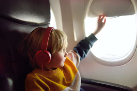 Cute little boy traveling by an airplane. Child using player to listen to a music or audiobook during the flight. Entertainment for family with kids on a board of planeの写真素材