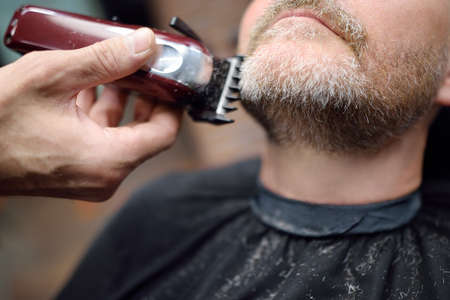 Barber master is shaving of handsome mature bearded man in salon. close-up. Hair artist making...