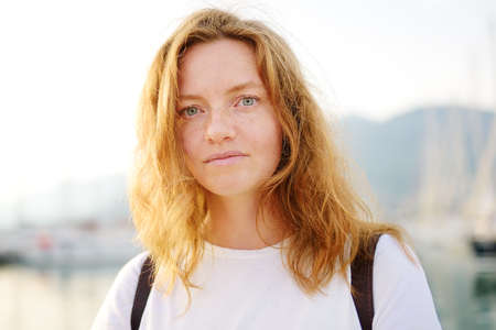Portrait of charming young tourist woman on the Mediterranean coast. Attractive red-haired girl hiking by the sea shore. Tourism, adventure and travel concept.の写真素材
