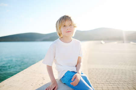 Portrait of cheerful smiling schoolboy child by sea during summer holidays on sunny day. Concept of freedom, happy childhood and limitless possibilities. Resort vacation for family with kidsの写真素材