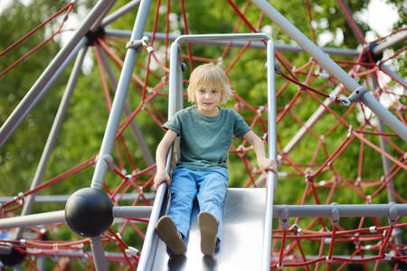 Cute little boy having fun on outdoor playground. Spring summer autumn active sport leisure for kids. Child on plastic slide. Equipment of entertainment park for kids.の写真素材