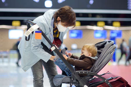 Young mother and toddler boy are in check-in desk at the airport. Child is sitting in a stroller....