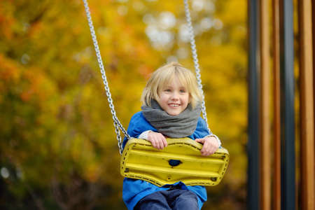 Little boy having fun on a swing on the playground in public park on autumn day. Happy child enjoy swinging. Active outdoors leisure for child in cityの写真素材