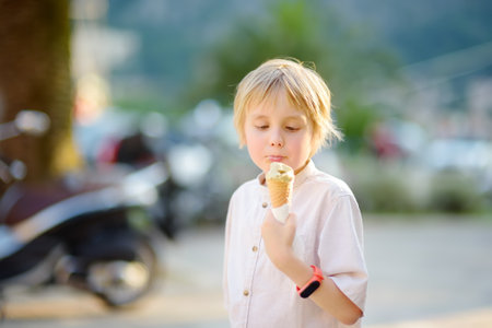 Little boy eating tasty ice cream cone outdoors during family stroll. Child have a snack on the go. Gelato is loved delicacy of kids. Sweets are unhealthy food for baby. Diabetes risk and obesity.の写真素材