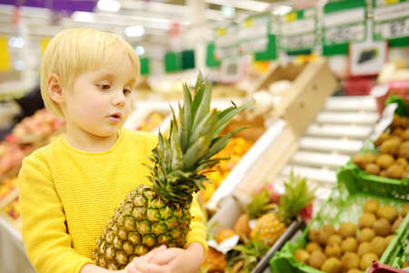 Cute toddler boy in a food store or a supermarket choosing fresh organic pineapple. Healthy lifestyle for young family with kidsの写真素材