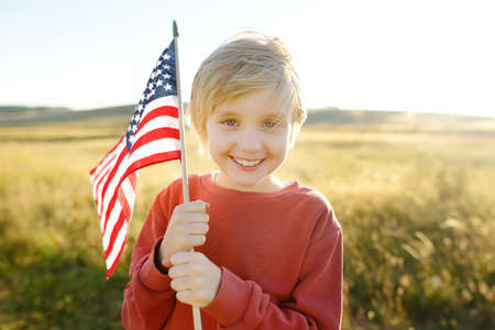 Cute little boy celebrating of July, 4 Independence Day of USA at sunny summer sunset. Child running and jumping with american flag symbol of United States over wheat field. pride and patriotismの写真素材