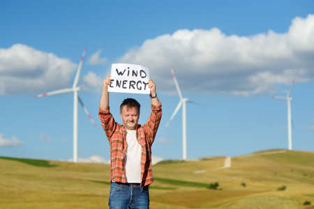 Eco activist with banner "Wind Energy" on background of power stations for renewable electric energy production. Person and windmills. Wind turbines for electricity generation. green concept energyの写真素材