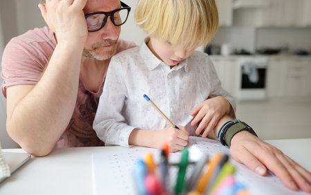 Tired father helping school boy with ADHD do his homework at home. Homeschooling, distance learning,...