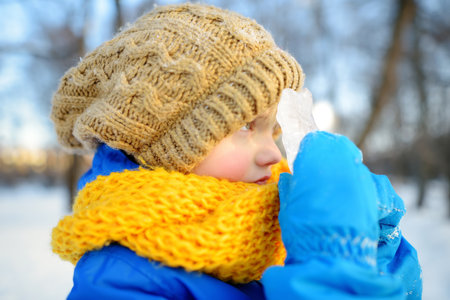 Little boy having fun playing with icicle in forest on sunny winter day. Baby looking through ice at...