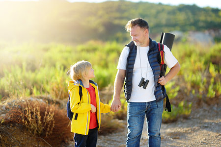 Cute schoolchild and his mature father hiking together and exploring nature. Child learning survival skills and orienteering. Concepts of adventure, scouting and hiking tourism for kids.の写真素材