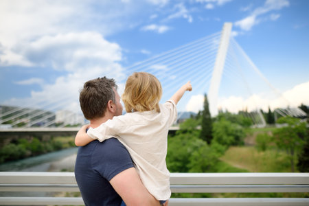 Little child and middle age father are admiring of cable stayed bridge. Boy is pointing of hand on Millennium bridge is above Moraca river in Podgorica, Montenegro. Family trip to Montenegroの写真素材