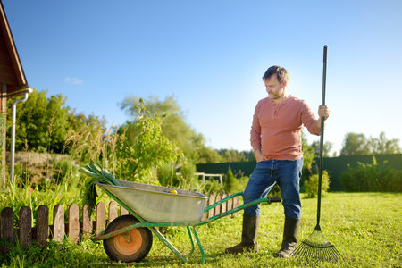 Handsome man farmer pushing wheelbarrow with freshly picked organic vegetables. Healthy vegetarian food. Harvesting. Veggies for sell. Small local businessの写真素材