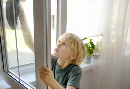 Cute little boy washing a window at home. Child helping parents with household chores, for example,...