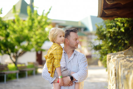 Preschooler boy with his dad are visiting outdoors petting zoo. Child having fun in farm with...