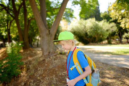 Elementary student boy with backpack, bottle of water and name badge on his neck goes to school. Happy child is waiting of school bus. Education for children.の写真素材