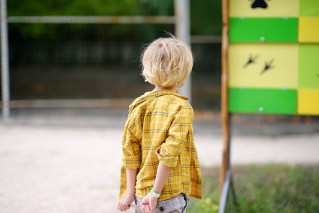 Little boy is visiting outdoors petting zoo. Child having fun in farm with animals. Children and animals. Entertainment for family with kids on school holidaysの写真素材