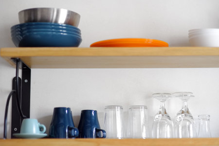 Dishware. Plates, bowls, mugs, cups, glasses are on a wooden shelfs. Kitchen accessories and utensil close-up.の写真素材