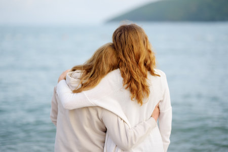 Redhead senior mother and her adult daughter are walking together on the sea shore. Happy loving mom and her grown up child embracing and admiring of nature.の写真素材