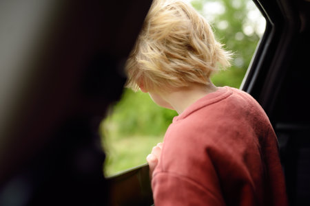 Cute preteen boy looking out through window of car during family road trip and enjoy of pleasant expectation of happy vacation. Joyful child travel with parents while holidays. Go everywhere.の写真素材