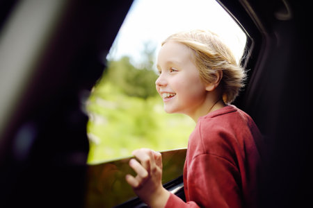 Cute preteen boy looking out through window of car during family road trip and enjoy of pleasant expectation of happy vacation. Joyful child travel with parents while holidays. Go everywhere.の写真素材