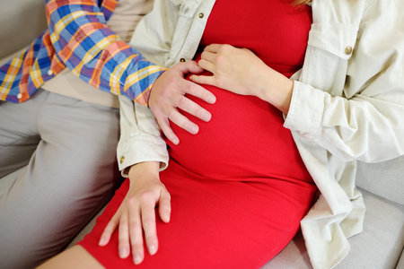 Happy couple is resting on the sofa at home. Young family is expecting a baby. Beautiful pregnant...
