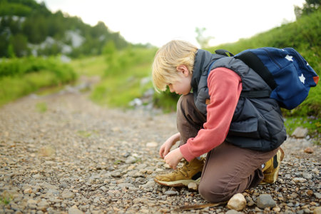 Preteen boy lacing up shoes while tracking on road in mountains valley. Family hiking with kids. Active lifestyle. Go everywhere concept.の写真素材