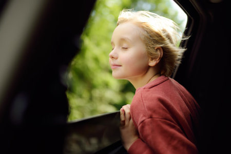 Preteen boy inhales the air of freedom from car window during family road trip and enjoy of pleasant...