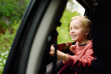 Cute preteen boy looking out through window of car during family road trip and enjoy of pleasant expectation of happy vacation. Joyful child travel with parents while holidays. Go everywhere.の写真素材