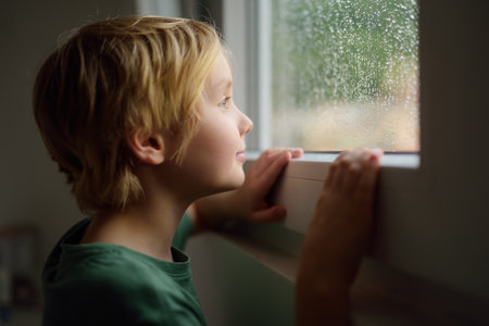 Portrait of preteen boy standing at the window. Child watching the rain outside. Faith and hope...