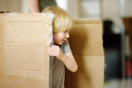 Cute preschool boy playing in a cardboard box during family's move to a new home. Kids play is a way of development of creative abilities. Entertainment for the child while the parents are busy.の写真素材