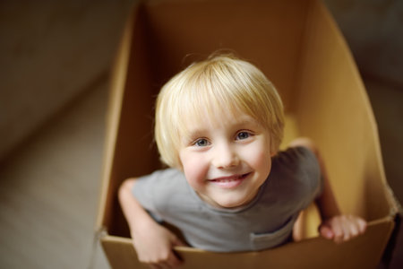 Cute preschool boy playing in a cardboard box during family's move to a new home. Kids play is a way of development of creative abilities. Entertainment for the child while the parents are busy.の写真素材