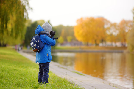 Little boy having fun during stroll in city park at sunny autumn day. Child exploring nature with binoculars. Active outdoor family time with kids. Beautiful modern urban park.の写真素材