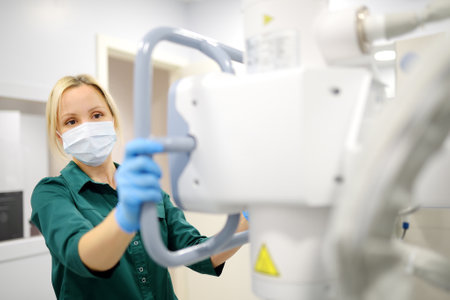 Female technician adjusts X-Ray machine. Female radiologist is going to take an Xray of patient in X-ray room of modern clinic. Medical examination of peopleの写真素材