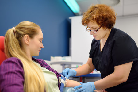 A nurse taking a blood from a young woman for examination in a modern laboratory or hospital. Young adult girl donor is at the time of donation processの写真素材