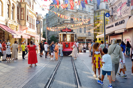 Istanbul, Turkey - August 5, 2023: Crowds of local people and tourists walking down the street Taksim Istiklal in district Beyoglu of Istanbul and admiring red retro tram on sunny summer day.のeditorial素材