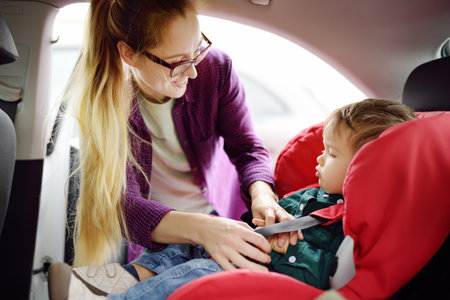 Caring mother fasten little baby in car seat. Young female preparing child for a trip. Safety of family travel by carの写真素材