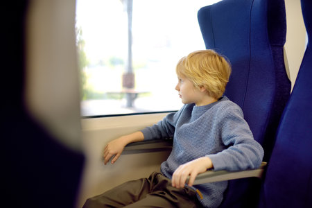 Cute preteen boy is traveling in a local train carriage or by railroad while it rains outside. Portrait of child passenger.の写真素材
